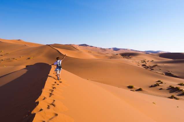 Traveller walking among red dunes in Sossusvlei, Namib Desert, Namibia